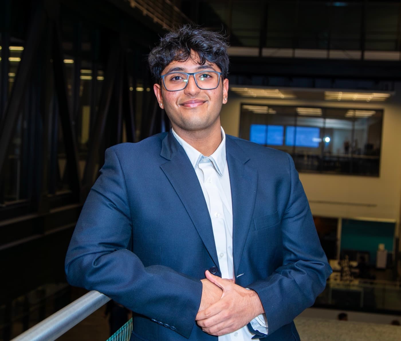 Aryan Bakshi in a navy suit, smiling in an office atrium — halftone print treatment